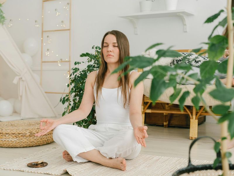 Person sitting in a meditative pose on a yoga mat in a minimalist room.